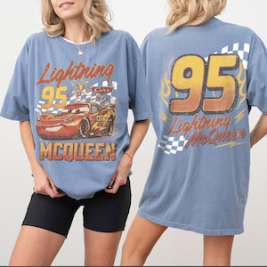 Może przedstawiać: Błękitna koszulka z Lightning McQueen z filmu Auta. Prz&oacute;d przedstawia samoch&oacute;d z napisem "Lightning 95 McQueen". Tył ma duży "95" i "Lightning McQueen" we wzorze płomieni.