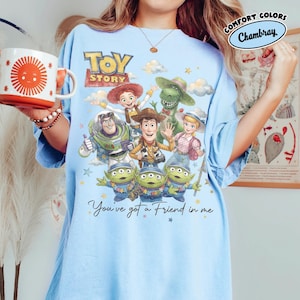May include: Pale blue t-shirt with a Toy Story graphic featuring Woody, Buzz Lightyear, and the aliens. The design includes the words "Toy Story" and "You've got a Friend in me". The shirt is made of a soft material and is a comfort fit.