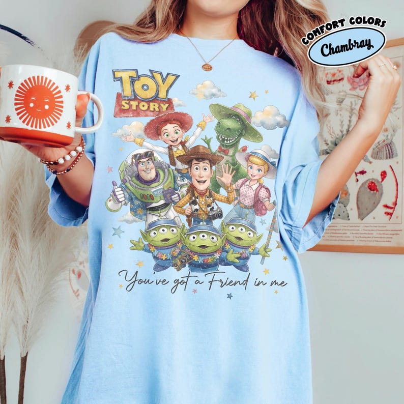 May include: Pale blue t-shirt with a Toy Story graphic featuring Woody, Buzz Lightyear, and the aliens. The design includes the words "Toy Story" and "You've got a Friend in me". The shirt is made of a soft material and is a comfort fit.