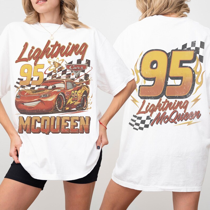 Może przedstawiać: Biała koszulka z grafiką Zygzaka McQueena z filmu Auta. Prz&oacute;d koszulki zawiera napis "Lightning 95 McQueen" i wizerunek samochodu. Tył koszulki ma duży napis "95" z napisem "Lightning McQueen" poniżej.