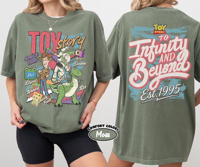 Pode incluir: Uma t-shirt verde musgo com gr&aacute;ficos de Toy Story. A frente mostra Woody, Buzz Lightyear, Rex e outras personagens com o texto "Toy Story Since 1995". As costas apresentam o log&oacute;tipo de Toy Story e o texto "To Infinity and Beyond Est. 1995".