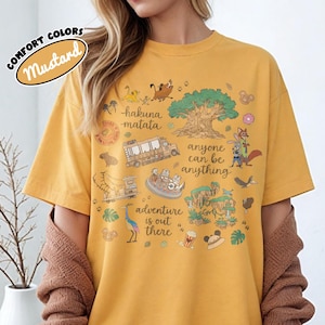 Puede incluir: Camiseta de color mostaza con un dise&ntilde;o gr&aacute;fico que presenta personajes de dibujos animados, un &aacute;rbol y las frases "hakuna matata" y "adventure is out there". La camiseta tambi&eacute;n tiene el texto "anyone can be anything."