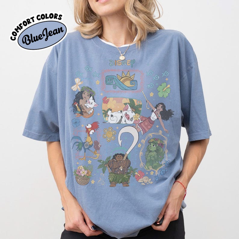 May include: A blue t-shirt featuring Disney's Moana characters. The design includes illustrations of Moana, Maui, Hei Hei, and Pua. The text "Comfort Colors Blue Jean" is printed on the upper left of the shirt.