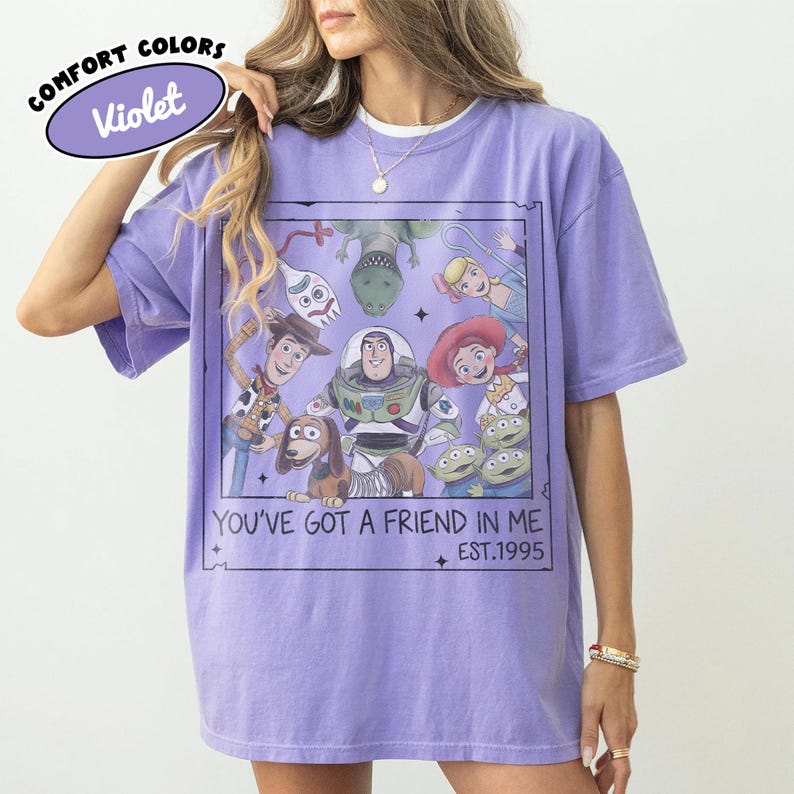May include: A violet Comfort Colors t-shirt featuring a graphic of Toy Story characters. The design includes Woody, Buzz Lightyear, and other characters with the text "YOU'VE GOT A FRIEND IN ME EST.1995".