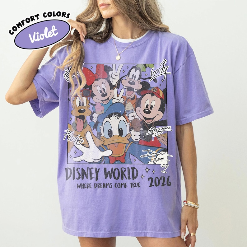 May include: Violet Comfort Colors t-shirt featuring a graphic of Disney characters including Mickey Mouse, Minnie Mouse, Donald Duck, and Goofy. The shirt has the text "Disney World 2026" and "Where Dreams Come True."