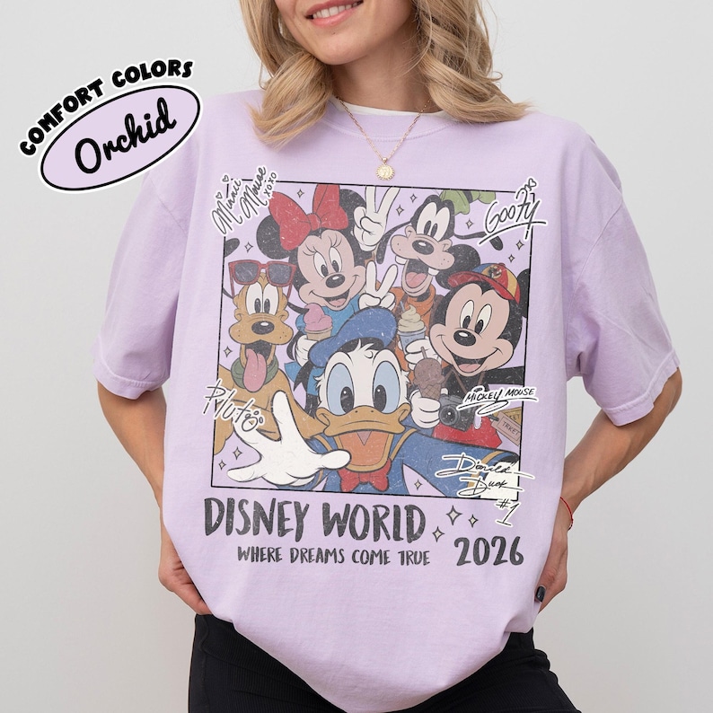 May include: Orchid-colored t-shirt featuring a Disney World graphic with Mickey Mouse, Minnie Mouse, Donald Duck, Goofy, and Pluto. The text "DISNEY WORLD" and "WHERE DREAMS COME TRUE 2026" are also visible. The shirt is a Comfort Colors brand.