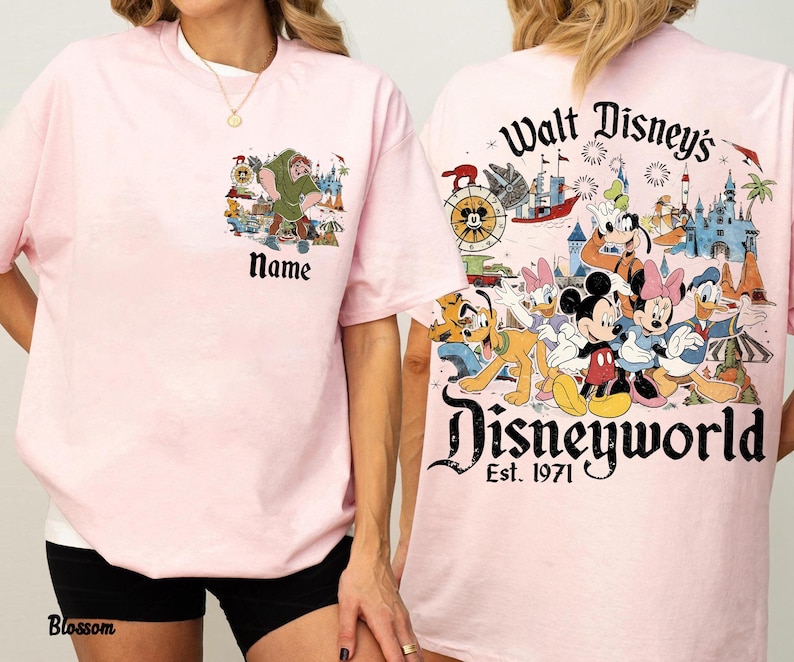 May include: Light pink t-shirts with Disney character graphics. One shirt features a cartoon scene with the text "Name", and the other displays "Walt Disney's Disneyworld Est. 1971" with various characters and a castle.
