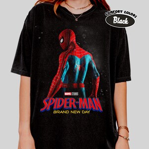 May include: Black t-shirt featuring a graphic of Spider-Man in a red and blue suit, with the text "SPIDER-MAN BRAND NEW DAY" in red and blue. The shirt also has the text "COMFORT COLORS Black".