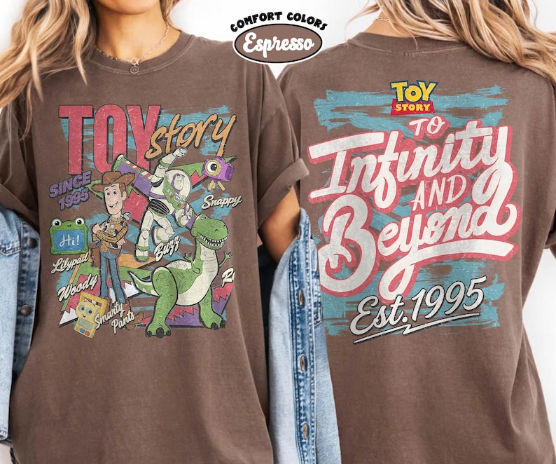 Pode incluir: Uma camiseta marrom de manga curta com gr&aacute;ficos de Toy Story. A frente mostra Woody, Buzz Lightyear, Rex e outros personagens com texto incluindo Toy Story, Since 1995 e nomes. As costas apresentam o texto To Infinity and Beyond.