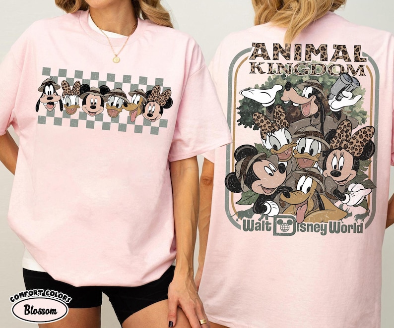 K&ouml;nnte beinhalten: Hellrosa T-Shirt mit einem Cartoon-Design von Disney-Figuren. Auf der Vorderseite befinden sich Gesichter von Figuren auf einem karierten Hintergrund. Auf der R&uuml;ckseite des Shirts stehen die Worte "ANIMAL KINGDOM" und "Walt Disney World".