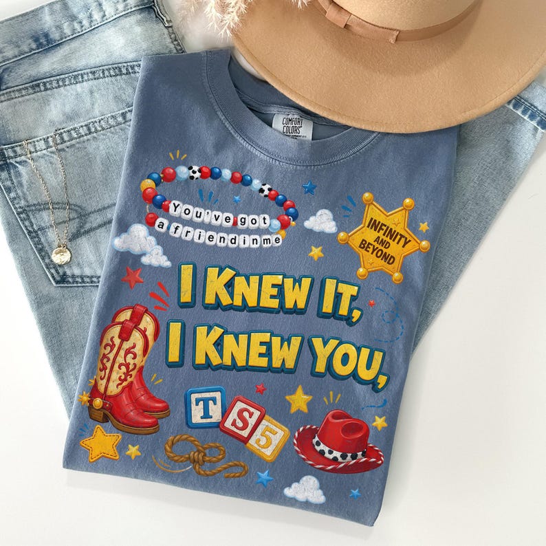 May include: A blue t-shirt featuring a graphic print with red cowboy boots, a red cowboy hat, a beaded bracelet with the text "You've got a friend in me," a yellow sheriff badge with "INFINITY AND BEYOND," and the text "I KNEW IT, I KNEW YOU."