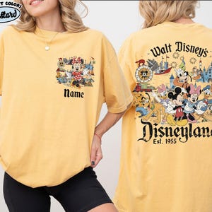 Peut inclure: T-shirt moutarde avec un th&egrave;me Disney. L'avant pr&eacute;sente un motif de Minnie Mouse avec le mot "Name" en dessous. Le dos affiche un design Disneyland avec des personnages Disney et le texte "Walt Disney's Disneyland Est. 1955."