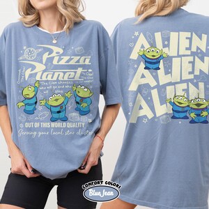 May include: Blue t-shirts with a Pizza Planet graphic on the front and Alien graphics on the back. The front design includes the text "Pizza Planet" and the phrase "Out of this world quality". The back features the word "Alien" repeated.