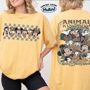 K&ouml;nnte beinhalten: Senfgelbes T-Shirt mit einer Grafik von Disney-Figuren, darunter Micky und Minnie Maus, Goofy und Donald und Daisy Duck. Auf der R&uuml;ckseite des Shirts steht "ANIMAL KINGDOM" und "Walt Disney World".