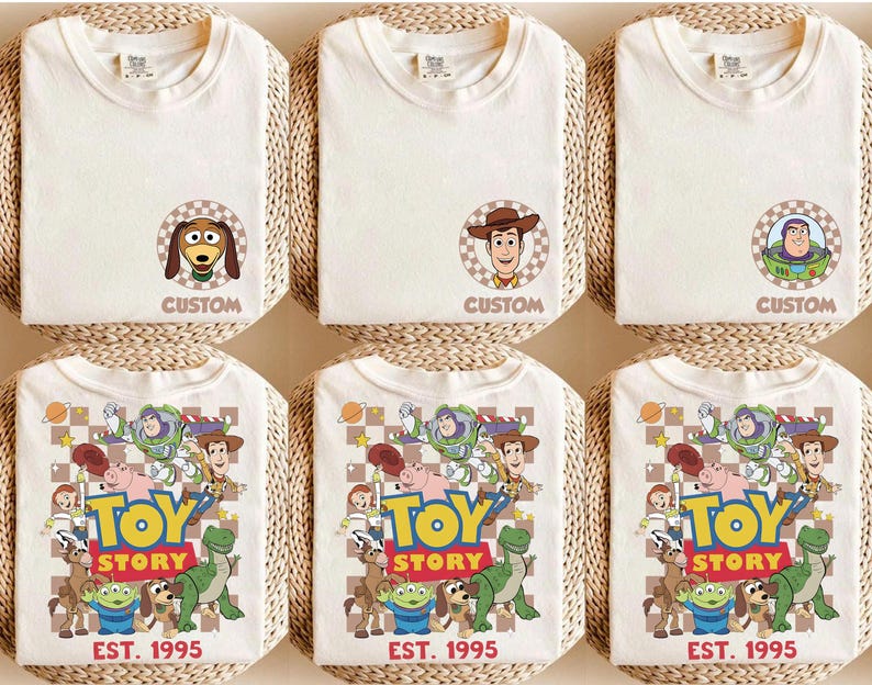 Puede incluir: Camisetas blanquecinas con personajes de Toy Story. Algunas camisetas tienen retratos de personajes con el texto "CUSTOM", mientras que otras muestran un gr&aacute;fico colorido con el texto "TOY STORY EST. 1995". Las camisetas est&aacute;n dobladas y colocadas sobre una superficie tejida.