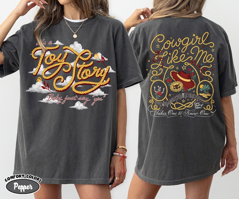 以下が含まれることがあります： チャコールグレーのTシャツ。フロントには白い雲の中に黄色いロープ風の文字で「it's a Toy Story」とプリントされています。バックには赤い帽子、ロープ、音符と共に「Cowgirl like me」という文字がデザインされています。