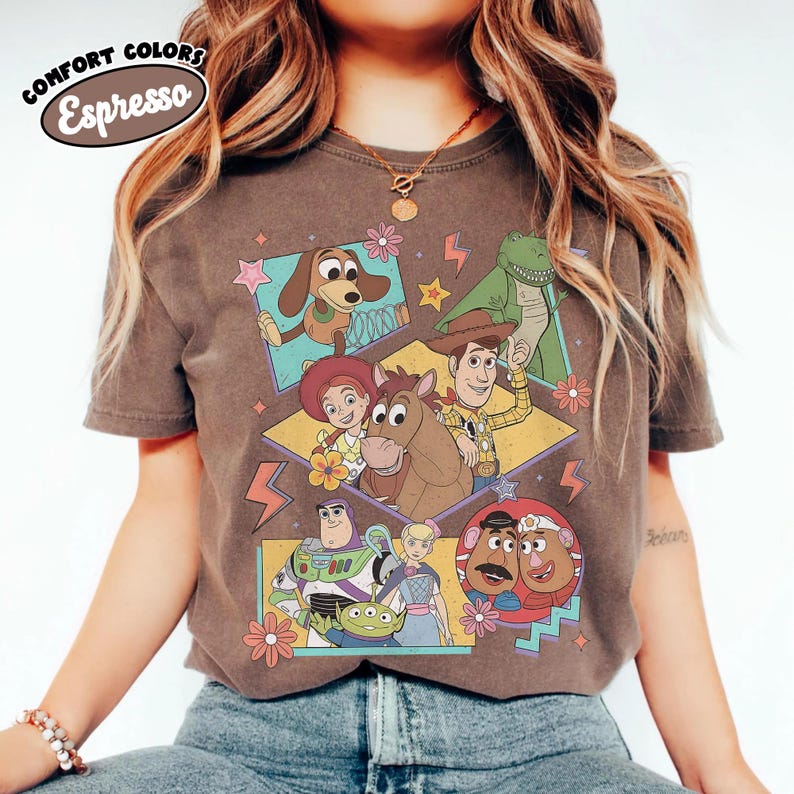 Puede incluir: Camiseta color espresso con un gr&aacute;fico de personajes de Toy Story. El dise&ntilde;o incluye a Woody, Buzz Lightyear y otros personajes en cajas coloridas con estrellas y flores. La camiseta tiene las palabras "COMFORT COLORS" y "Espresso" en un dise&ntilde;o circular.