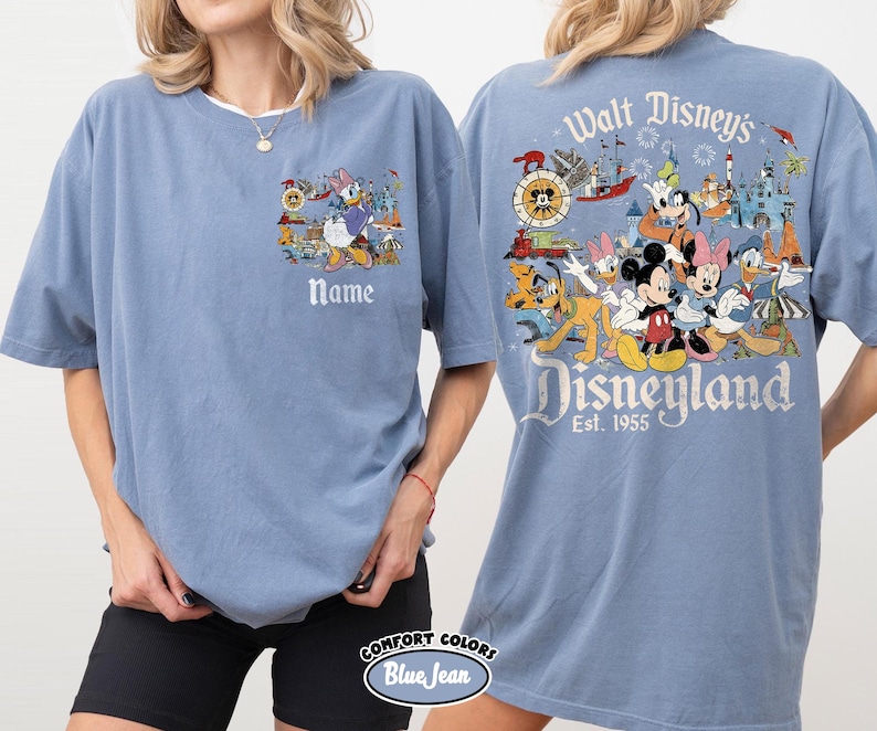 Peut inclure: Un t-shirt bleu Comfort Colors avec un motif Disneyland. Le devant pr&eacute;sente Daisy Duck et le mot "Name". Le dos affiche Mickey Mouse, Minnie Mouse et d'autres personnages Disney avec les mots "Walt Disney's Disneyland Est. 1955".