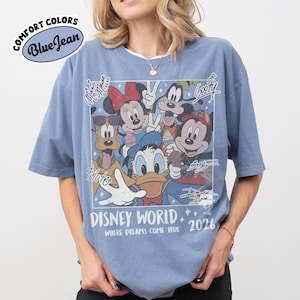 May include: Blue jean Comfort Colors t-shirt featuring a Disney World graphic with Mickey Mouse, Minnie Mouse, Donald Duck, Goofy, and Pluto. The graphic includes the text "Disney World 2026" and "Where Dreams Come True."