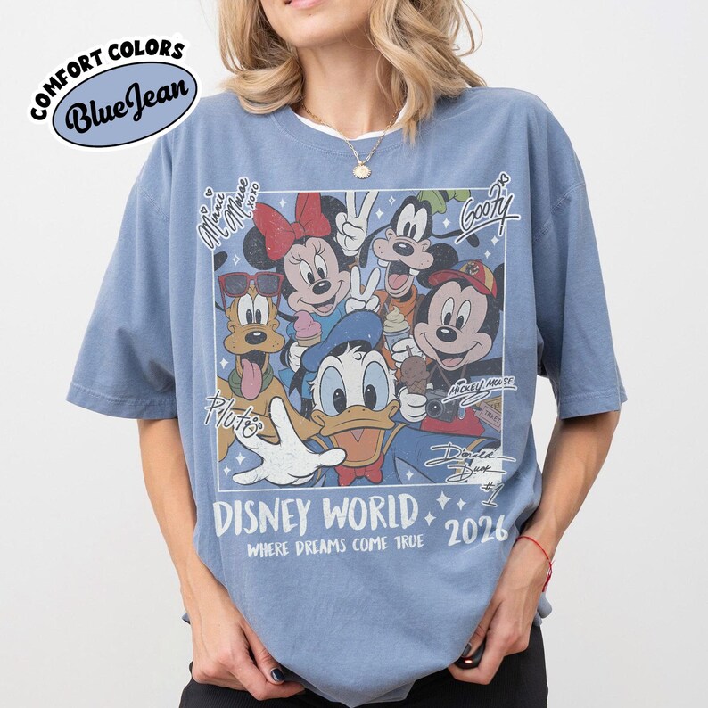 May include: Blue jean Comfort Colors t-shirt featuring a Disney World graphic with Mickey Mouse, Minnie Mouse, Donald Duck, Goofy, and Pluto. The graphic includes the text "Disney World 2026" and "Where Dreams Come True."
