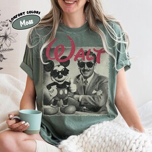 K&ouml;nnte beinhalten: Moosgr&uuml;nes T-Shirt mit einem Vintage-Grafik von Mickey Mouse und Walt Disney mit Sonnenbrille, mit dem Wort "WALT" in Rot. Das Shirt ist von der Marke Comfort Colors.