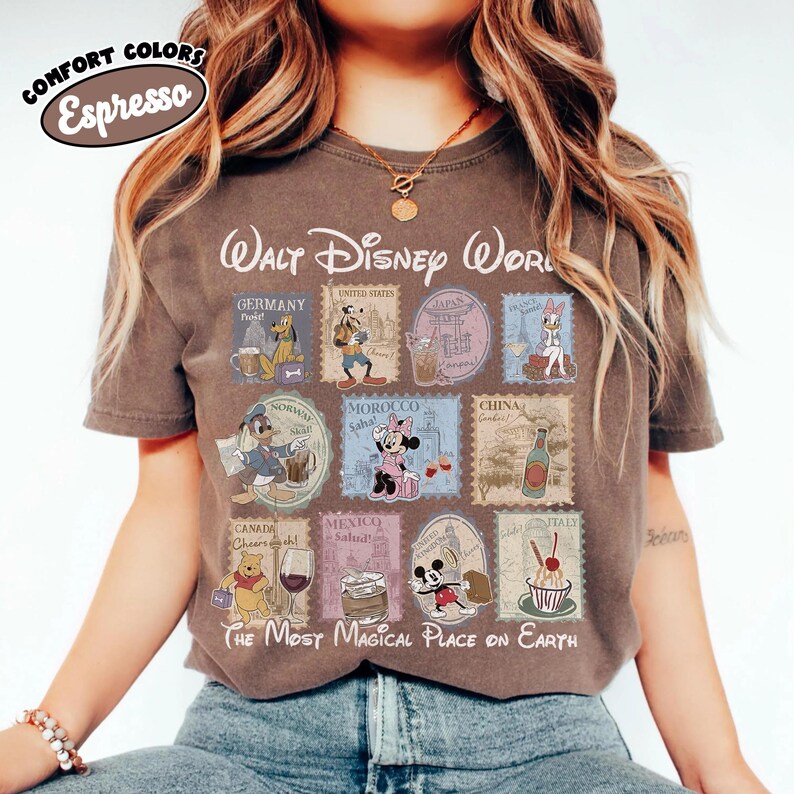 May include: Espresso-colored t-shirt featuring a Walt Disney World design. The shirt showcases various Disney characters and stamps representing different countries. Text includes "The Most Magical Place on Earth."