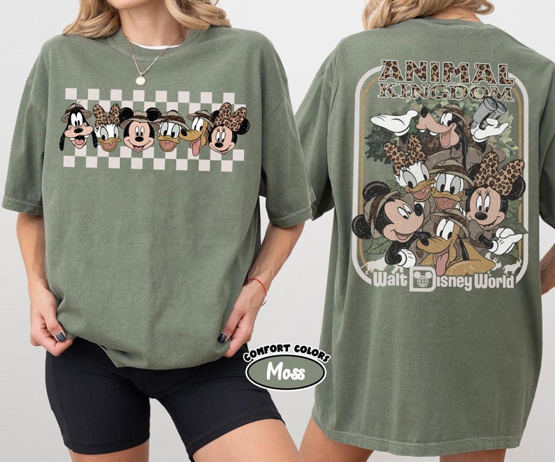 K&ouml;nnte beinhalten: Olivgr&uuml;nes T-Shirt mit einer Grafik von Disney-Figuren, darunter Micky Maus, Minnie Maus, Donald Duck und Goofy, mit einem Schachbrettmuster. Auf der R&uuml;ckseite des Shirts stehen die Worte "Animal Kingdom" und "Walt Disney World".