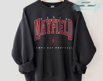 Puede incluir: Sudadera negra con el nombre "MAYFIELD" en letras rojas con contorno blanco. La palabra "BAKER" está encima del nombre, y "TAMPA BAY FOOTBALL" está debajo. Un escudo con el número "6" está en el centro.