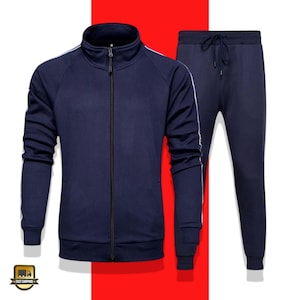 Könnte beinhalten: Marineblaues Trainingsanzug-Set. Die Jacke hat einen durchgehenden Reißverschluss, einen Stehkragen und weiße Streifen an den Ärmeln. Die passende Hose hat einen Kordelzug in der Taille. Das Set wird vor rotem und weißem Hintergrund gezeigt.