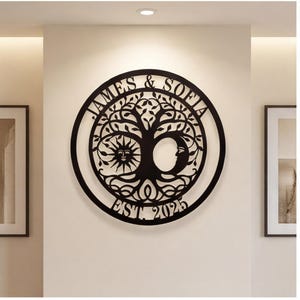 May include: A circular black metal wall art piece featuring a tree of life design with a sun on the left and a crescent moon on the right. The text JAMES & SOFIA is arched at the top, and EST. 2025 is arched at the bottom within the circular frame.