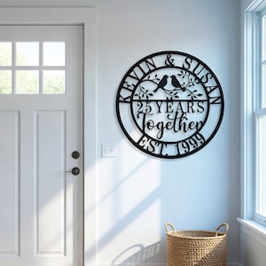 May include: Black metal wall art with the names "KEVIN & SUSAN" and the text "25 YEARS Together EST. 1999" in a circular design. Two birds perch on a branch. The art is mounted on a white wall near a door.