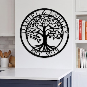Puede incluir: Un letrero de pared circular de metal negro con la silueta detallada de un árbol con pájaros posados en las ramas. El texto DANIEL & ASHLEY está arqueado en la parte superior y EST. 2019 está centrado en el borde inferior del marco.