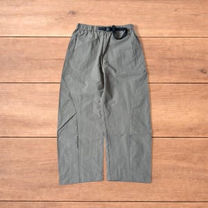 May include: Olive green trousers with a black belt. The trousers have a relaxed fit, pockets, and a drawstring waistband. The fabric appears lightweight, suitable for casual wear.