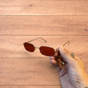 Occhiali da sole polarizzati con montatura in metallo color oro e lenti rosse.