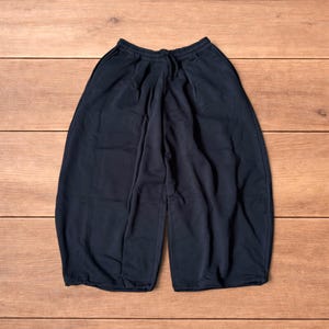 Könnte beinhalten: Eine einfarbige, schwarze Hose mit weitem Bein, einem bequemen elastischen Bund und einem passenden Kordelzug. Diese locker sitzende Hose hat eine verkürzte Länge und eine entspannte Silhouette mit tiefen Falten im gesamten Stoff.