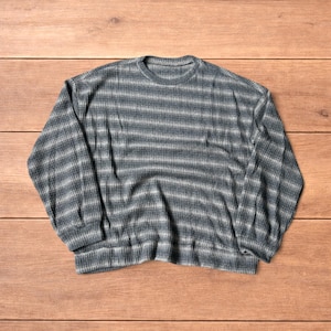 Puede incluir: Un suéter de manga larga con cuello redondo que presenta un patrón de punto texturizado con rayas horizontales alternas en tonos gris carbón, gris pizarra y blanco, acabado con puños y dobladillo acanalados en el borde inferior.