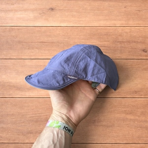 Puede incluir: Gorra azul bígaro para actividades al aire libre con visera curva. La gorra tiene la palabra "outdoor" impresa en un lateral. Fabricada con un material ligero, ideal para actividades al aire libre.