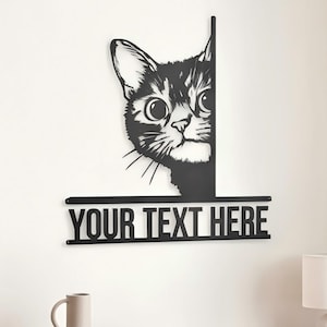 May include: A black metal wall art piece featuring a cat peeking from behind a vertical edge. Below the cat, a horizontal bar displays the text YOUR TEXT HERE in bold, capital letters. The design is flat, silhouette-style, and mounted on a wall.