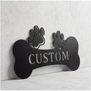 May include: Black metal dog bone-shaped sign with the word "CUSTOM" cut out. Two paw prints are above the bone. The sign is mounted on a light gray textured wall.