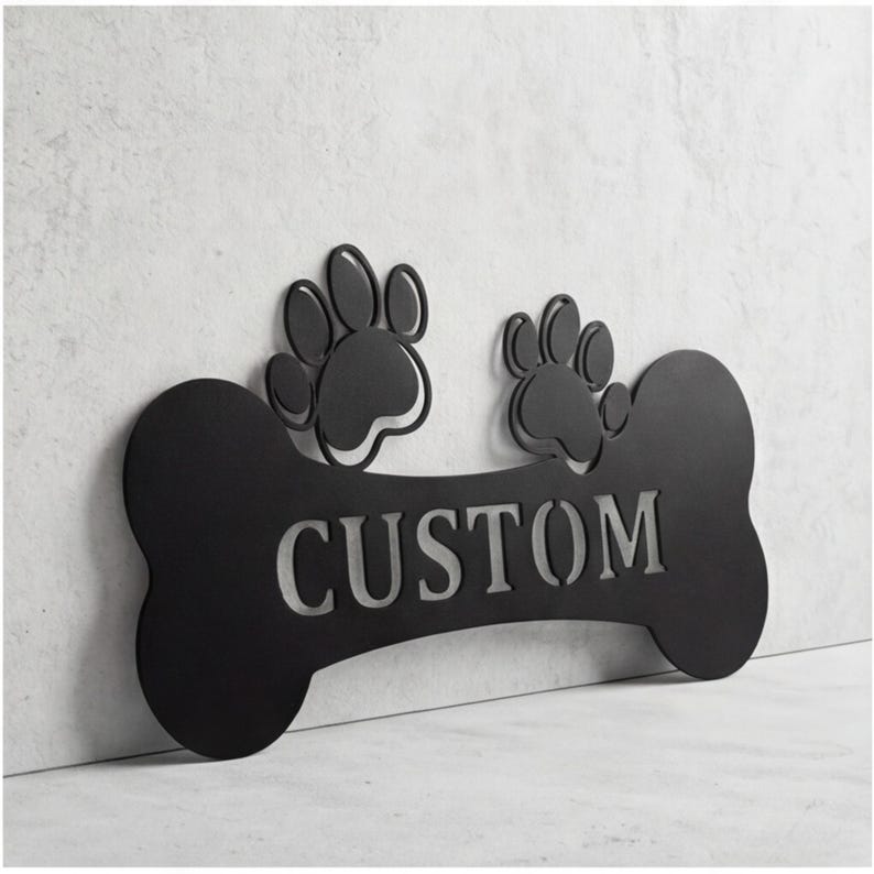 May include: Black metal dog bone-shaped sign with the word "CUSTOM" cut out. Two paw prints are above the bone. The sign is mounted on a light gray textured wall.