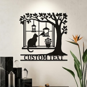 May include: A black metal wall art piece featuring a silhouette of a cat sitting on a window ledge next to a potted flower and a bird feeder. A tree with leaves hangs over the window, and the words CUSTOM TEXT are displayed at the bottom.