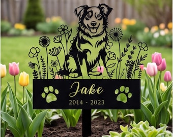 May include: A black metal garden stake featuring a silhouette of a dog sitting among wildflowers. The rectangular base displays the name Jake in script font, the dates 2014-2023, and two paw print cutouts on either side of the text.