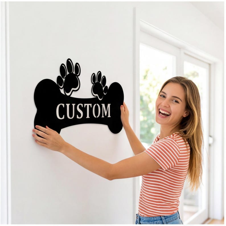 May include: Black bone-shaped sign with the word "CUSTOM" in white lettering. Two paw prints are above the word. The sign is being held up against a white wall.