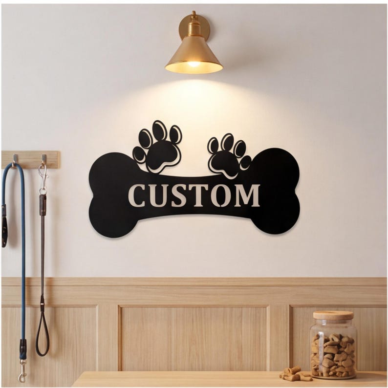 May include: Black bone-shaped sign with the word "CUSTOM" in white, topped with two paw prints. The sign is mounted on a white wall, with a gold-colored light fixture above. Dog leashes hang on the left.