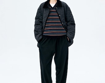 May include: A black quilted jacket with a dark collar worn over a V-neck sweater featuring horizontal stripes in blue, gray, and orange patterns, paired with loose-fitting black trousers and black loafers.