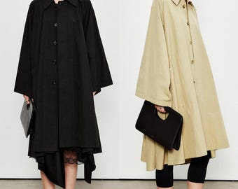Può includere: Due donne indossano lunghi cappotti abbottonati. Uno è nero, l'altro beige. Entrambe le modelle tengono in mano borse nere. Il cappotto nero è abbinato a una gonna nera con finiture in pizzo, mentre il cappotto beige è indossato con leggings neri.
