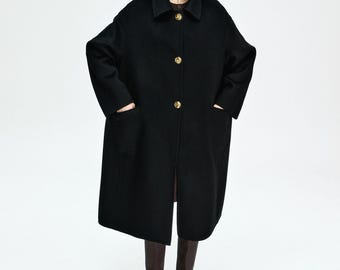 Può includere: Un cappotto lungo nero con grandi bottoni dorati e tasche anteriori. Il cappotto ha un colletto classico e un orlo al ginocchio. La modella indossa stivali marroni. Il cappotto è un'elegante opzione di capospalla.