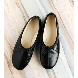 Puede incluir: Una taza de cerámica blanca con un asa negra y el texto "But First, Coffee" en negro, con una fuente de estilo manuscrito. La taza está sobre una superficie blanca.