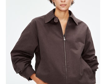 Puede incluir: Chaqueta marrón oscuro con cuello y cierre de cremallera. La chaqueta tiene mangas largas y se combina con unos vaqueros azules. La modelo lleva la chaqueta y mira a la cámara.