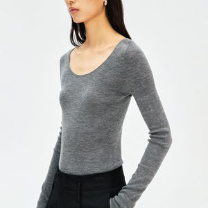 May include: A long-sleeved, heather grey knit top featuring a wide, rounded scoop neckline. The garment is constructed from a fine-gauge, lightweight material that fits closely to the torso and arms, ending in straight, unbanded cuffs at the wrists.